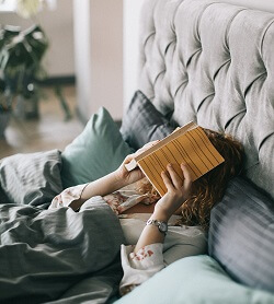 A woman lying in bed with a book covering it