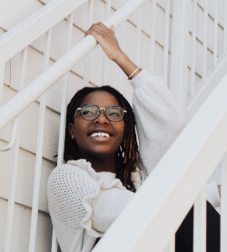 A woman smiling while sitting on an outdoor staircase. Practicing mindfulness can help you better understand your emotions, and thereby learn to be happier.