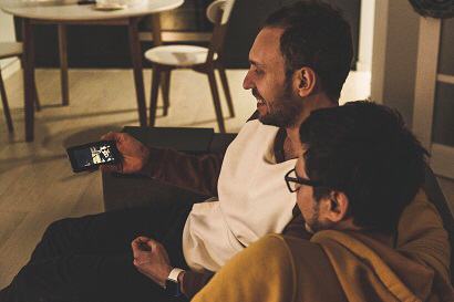 Two men on the couch watching a video on the phone. Little distractions like this are a good way to prevent the worst of stress.