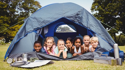 7 Kinder liegen in einem Zelt und freuen sich: Campingplatz-Urlaub boomt in der Corona-Zeit. Gut geschützt mit einer Camping-Reiseversicherung der ERGO.