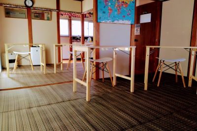 木製の机と白い椅子が並ぶ英会話教室の室内。壁には世界地図と時計がかかっている