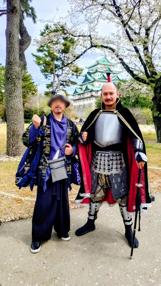 リラクゼーションサロン「forest hands（フォレストハンズ）」のセラピスト・徹平が、桜が咲く名古屋城を背景に、甲冑を身にまとった織田信長（名古屋おもてなし武将隊）と並んで力強くガッツポーズをしているツーショット写真。