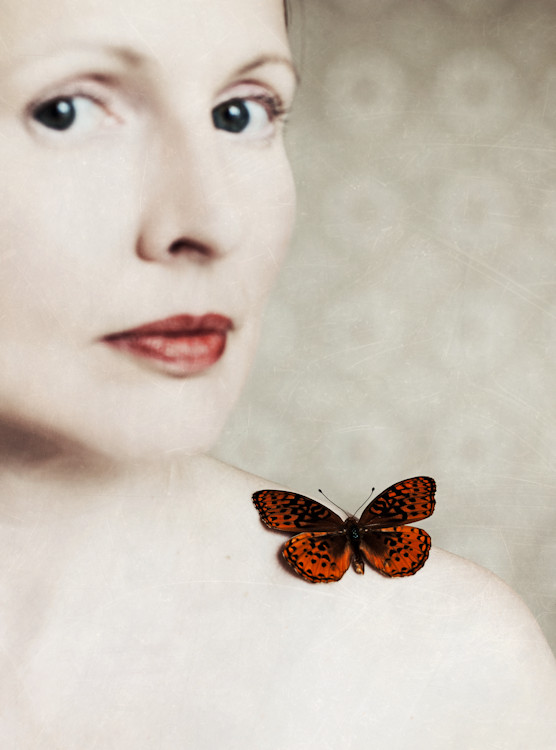 Manuela Deigert Projekte A touch of vintage, Selbstportrait mit einem Schmetterling auf der Schulter, im Hintergrund eine gemusterte Tapete im Vintage Stil