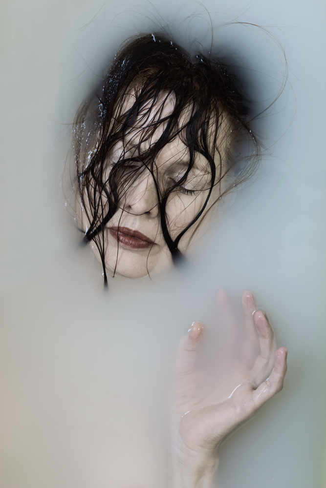 Manuela Deigert Bildsprache Selbstportrait im Milchbad mit dunklen Haaren vor dem Gesicht