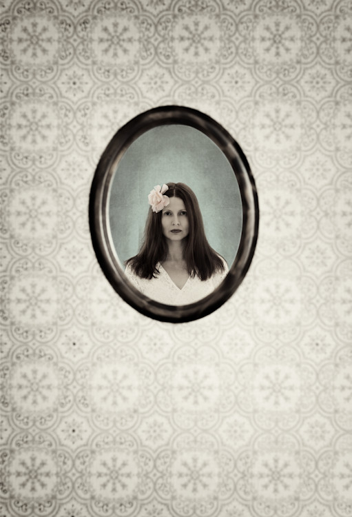 Manuela Deigert Projekte A touch of vintage, Spiegelbild von einer schönen Frau mit Blume im Haar an einer Wand mit gemusterter Tapete im Vintage Stil