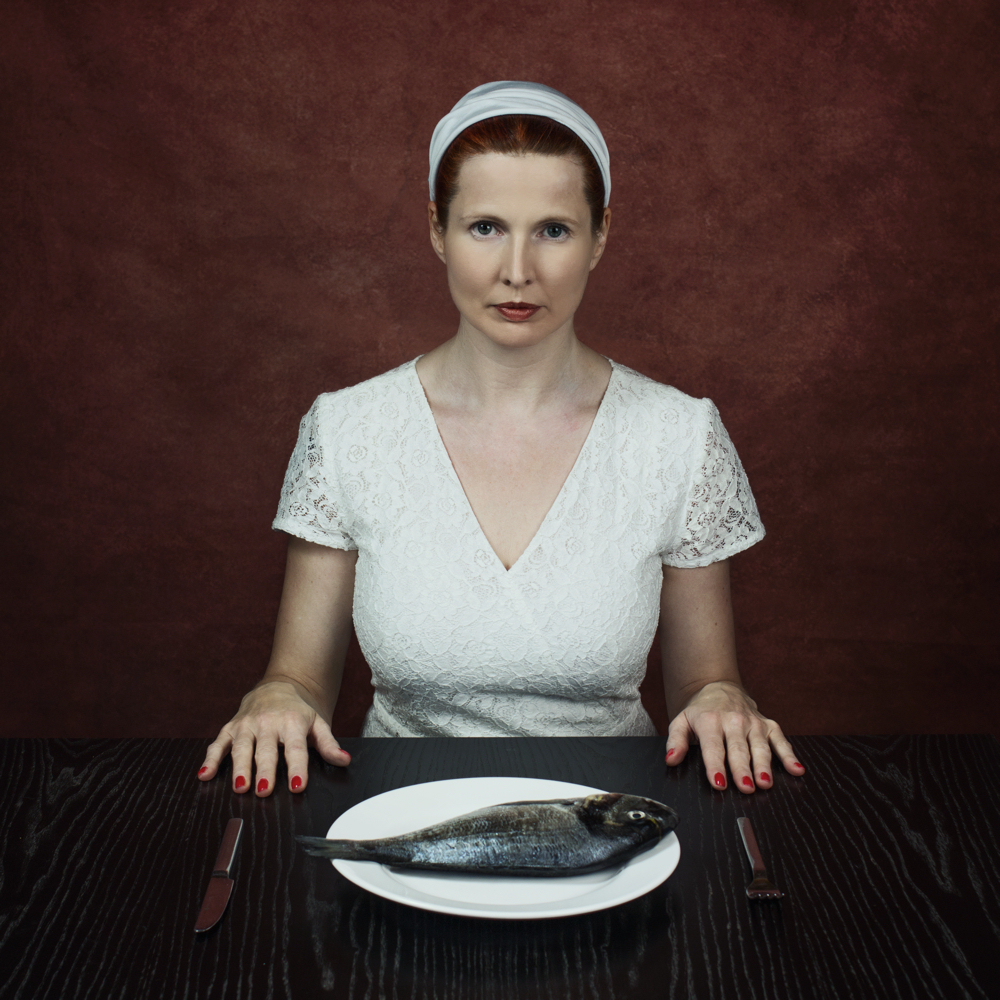 Manuela Deigert Projekte Frau sitzt an einem Fisch mit einem Teller auf dem eine Dorade liegt