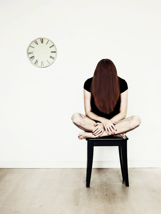 Manuela Deigert Bildsprache, melancholisches Selbstportrait im Schneidersitz auf einem Hocker sitzend, an der Wand eine Uhr ohne Zeiger