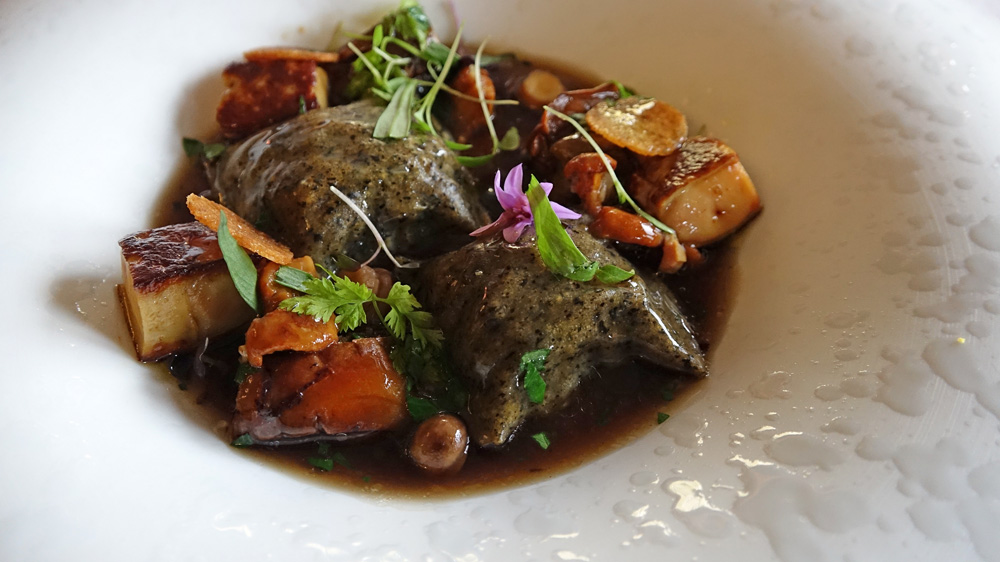 Raviole de champignons aux herbes potagères, cèpes et foie gras servis dans un léger bouillon de champignons de Paris relevé à l'huile d'ail