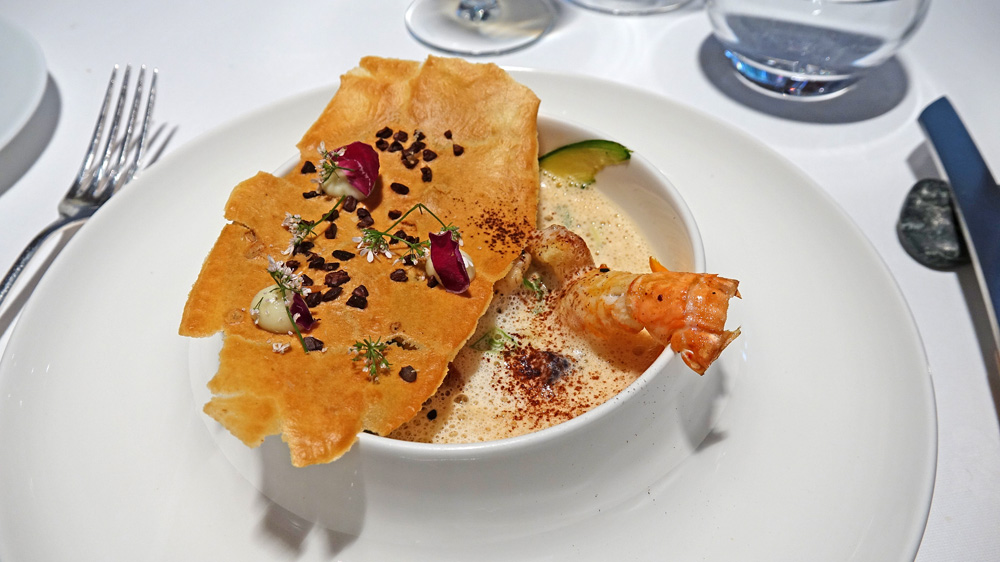 Raviole de crevettes sauvages, langoustine rôtie et tuile au gué de cacao, cacao en poudre.