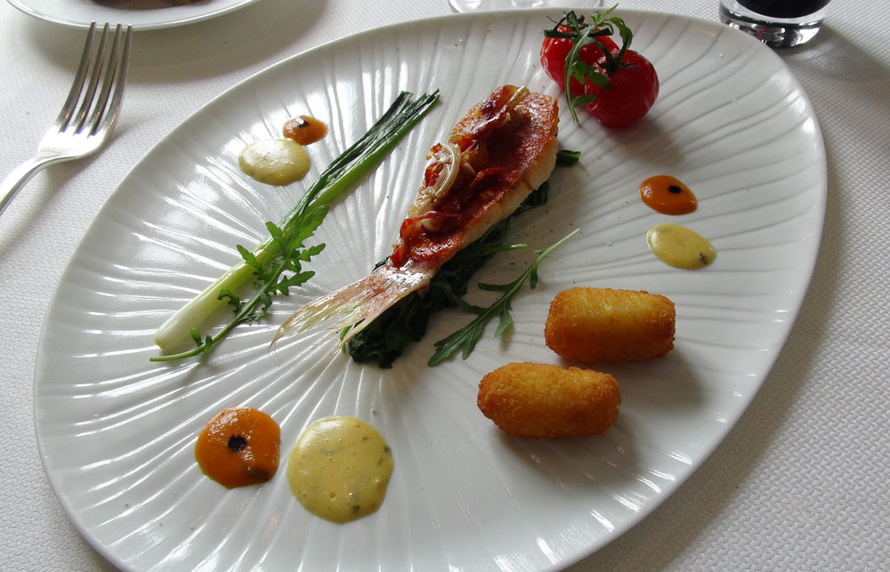 et un Filet de rouget-barbet, roquette sauvage, croquettes de pomme de terre au lard fumé, tomates confites et croustillance de cochonnaille