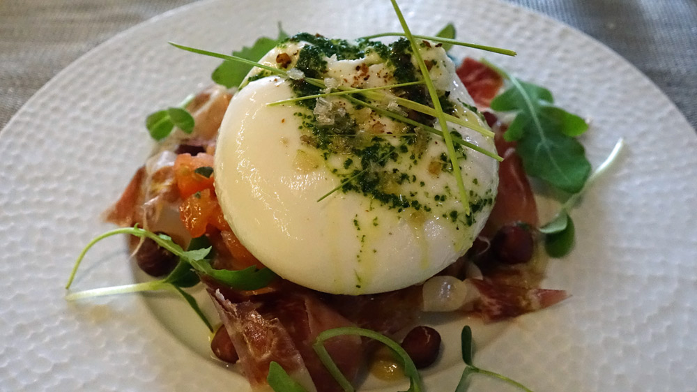 Burrata de bufflonne servie sur un blinis tiède aux noisettes, brunoise de tomates, copeaux de paletta ibérique et roquette