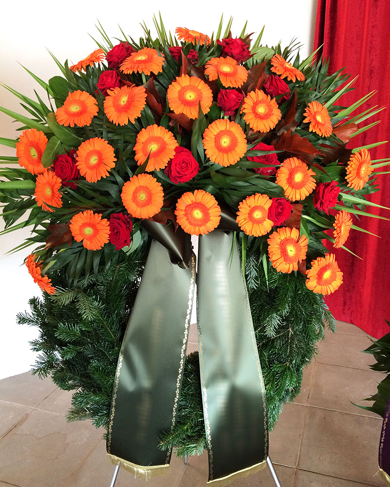 Trauerkranz mit orangen Gerbera, roten Rosen und gemischtem Grün.