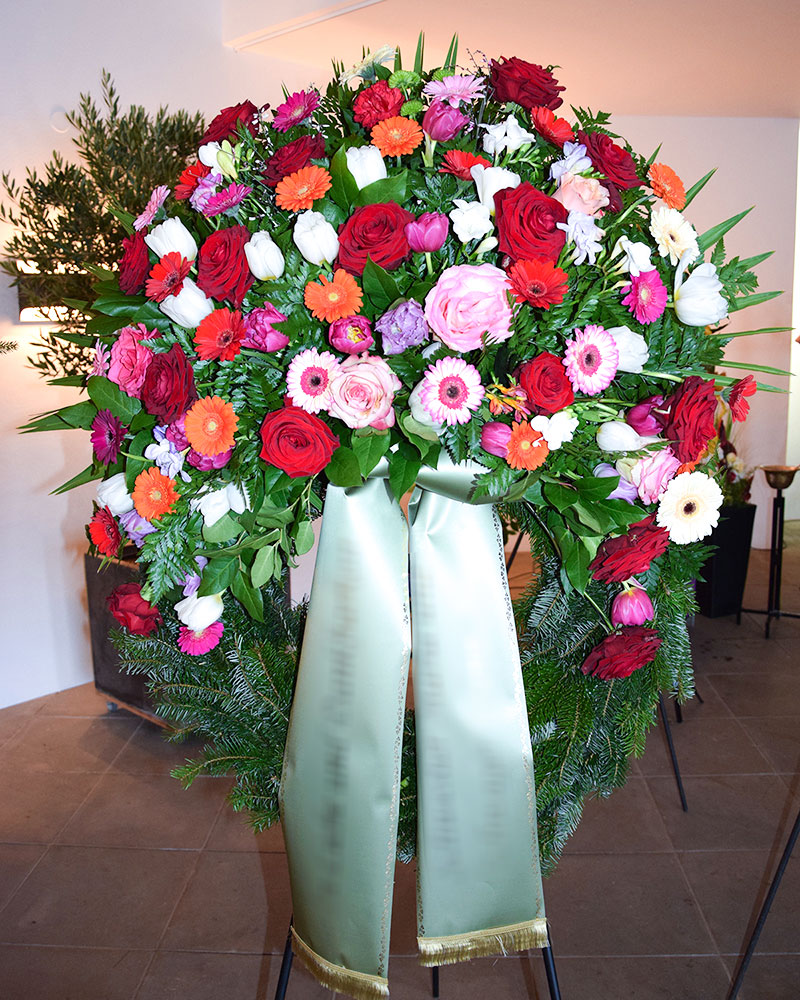 Trauerkranz mit bunten Germini, bunten Rosen, bunten Tulpen und gemischtem Grün.