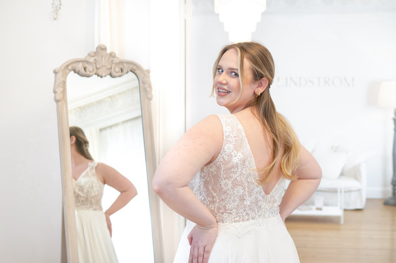 Glückliche Curvy-Braut bei der Anprobe ihres Brautkleides vor dem Spiegel in Homburg.