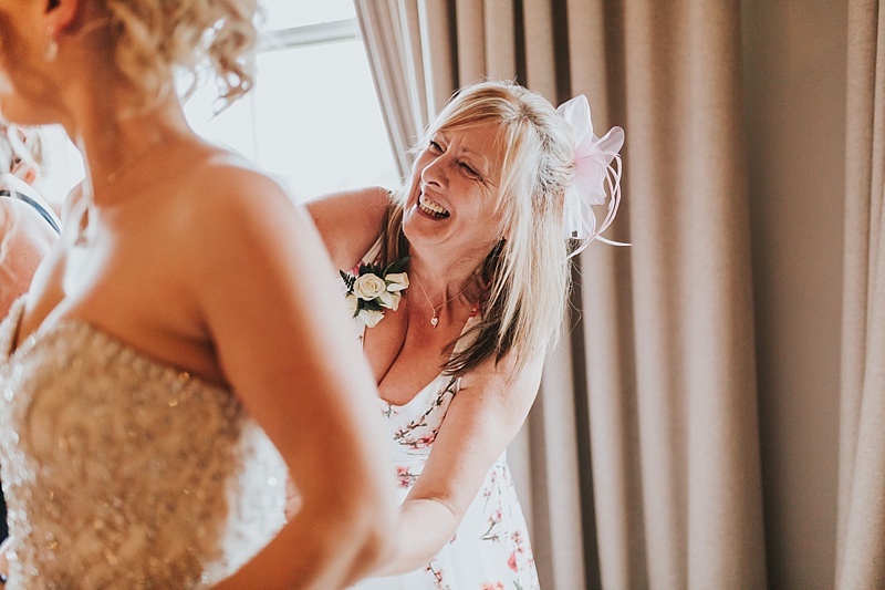 mother of the bride laughing as she zips up her daughters wedding dress