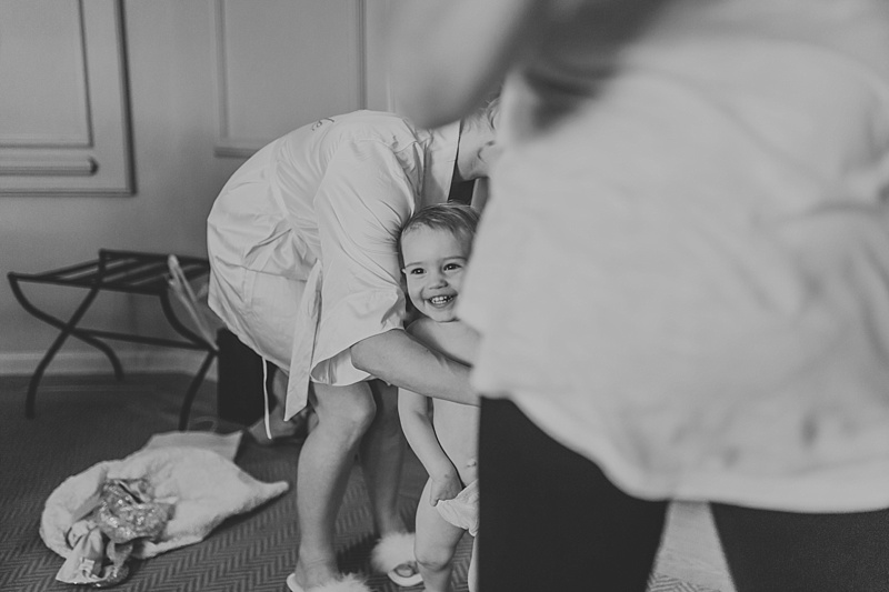 cheeky little flower girl laughing as her mum is trying to dress her