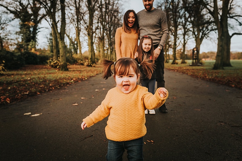 cute little girl in a mustard jumper running towards camera during family portraits