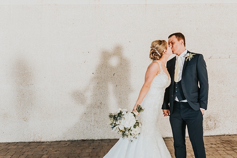Cute portrait of a bride and groom kissing with their shadows behind them on a wall