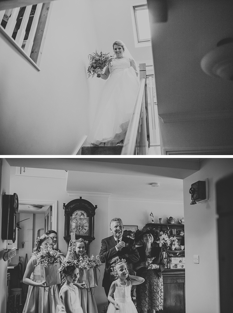 bride walking down the stairs on her wedding day whilst her parents and bridesmaids look with excitement