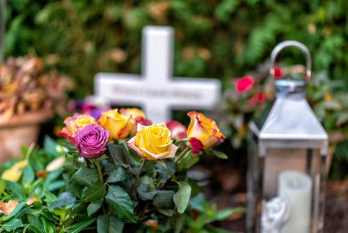 Bunte Rosen am Grab vor einem Kreuz