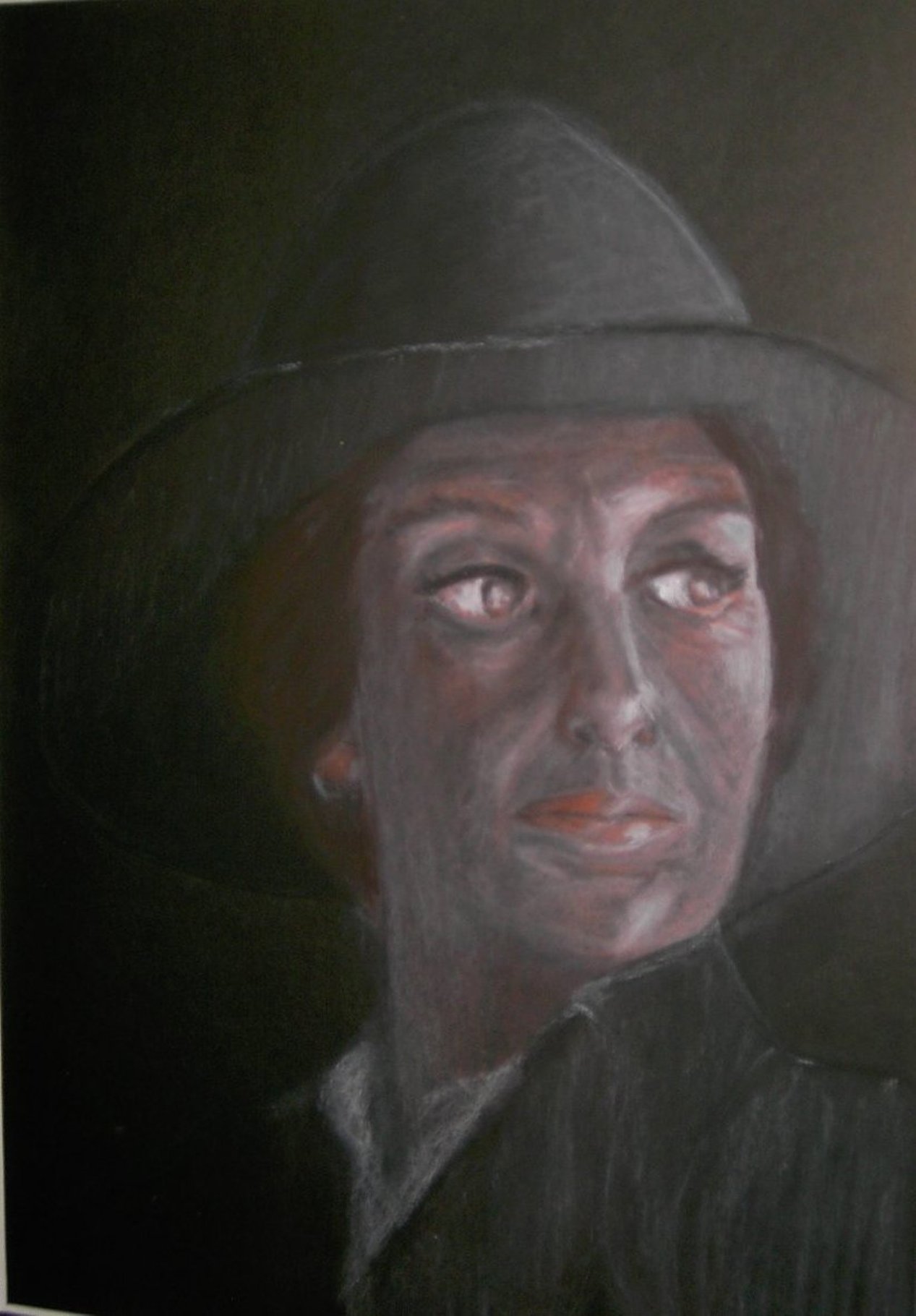 Zeitgenössische Malerei von Alexandra Mohr: Ein Portrait einer Frau mit Hut, die melancholisch nach rechts schaut, gemalt mit Rötel und Kreide auf schwarzem Karton. Das war eine Auftragsarbeit.
