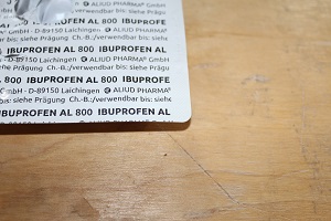 Dieses Farbfoto von Thorsten Hülsberg zeigt einen angebrochenen Ibuprofenfilm auf einem Holztisch.