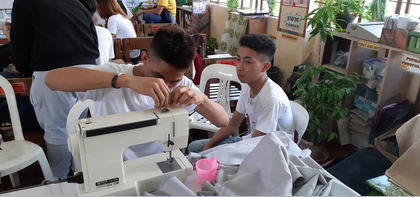 Straßenjungs in Manila lernen mit der Nähmaschine umzugehen