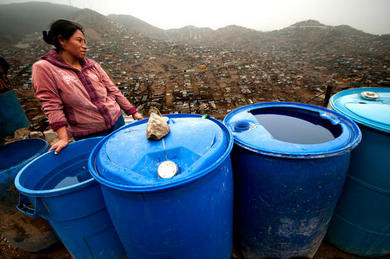 A woman in Pamplona Alta, Lima - Peru, beside the big blue drums they use to fill with potable water that trucks deliver to them each of two days. This water is at least 4 times more expensive that water that usually people have at home.