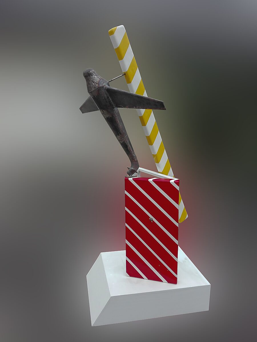 Gelovige vliegtuigen — zijaanzicht van een metalen vliegtuig dat schuin omhoog helt boven een rood gestreepte steunstructuur, waarbij het object balanceert tussen industriële vorm en sculpturale compositie.
