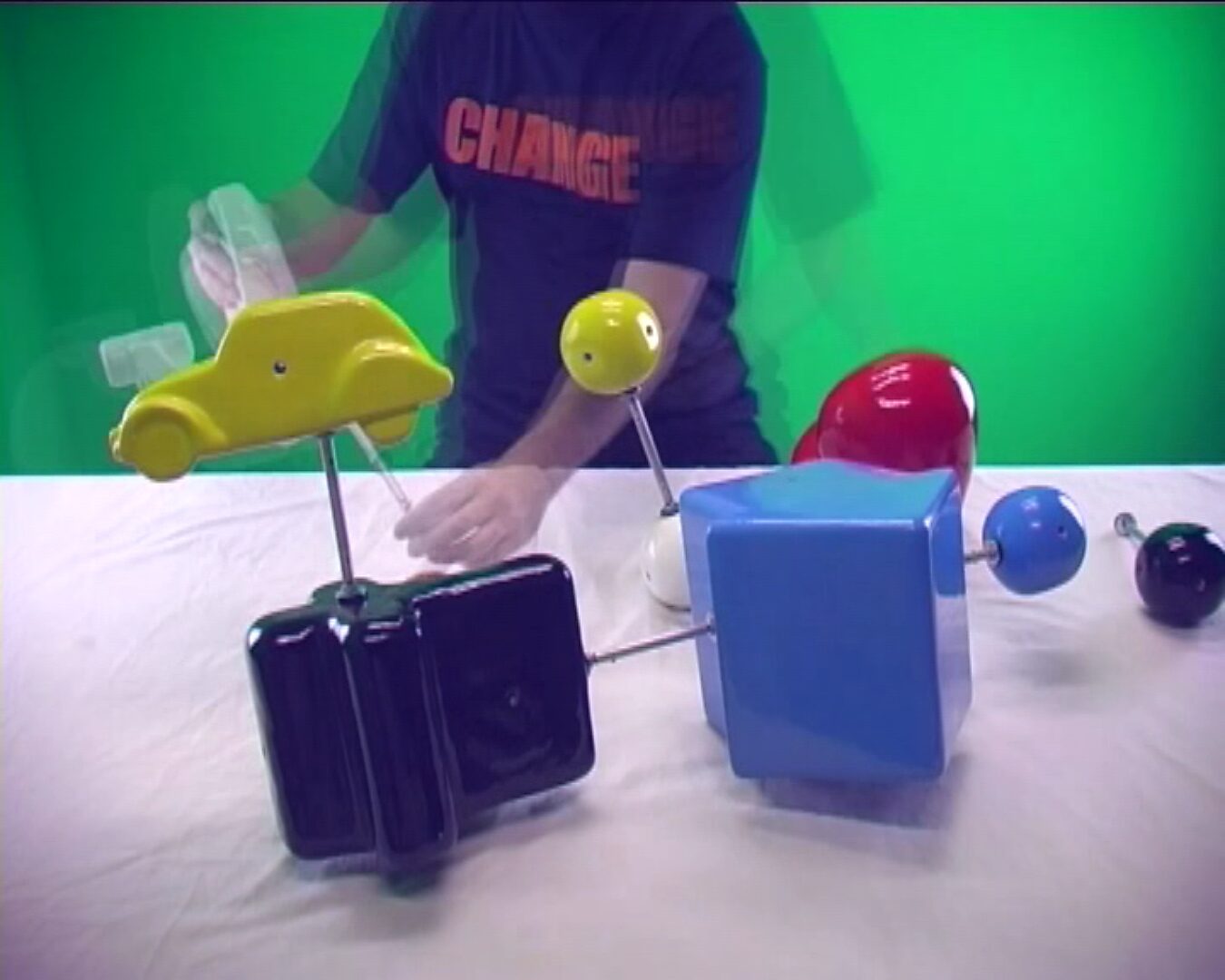 ChooseChoose and Change no. 1 — video still of a demonstration where multiple forms come together into a temporary assembly on a table. and Change no. 1 — video still of a demonstration where yellow, black and blue forms on rods are combined and moved.
