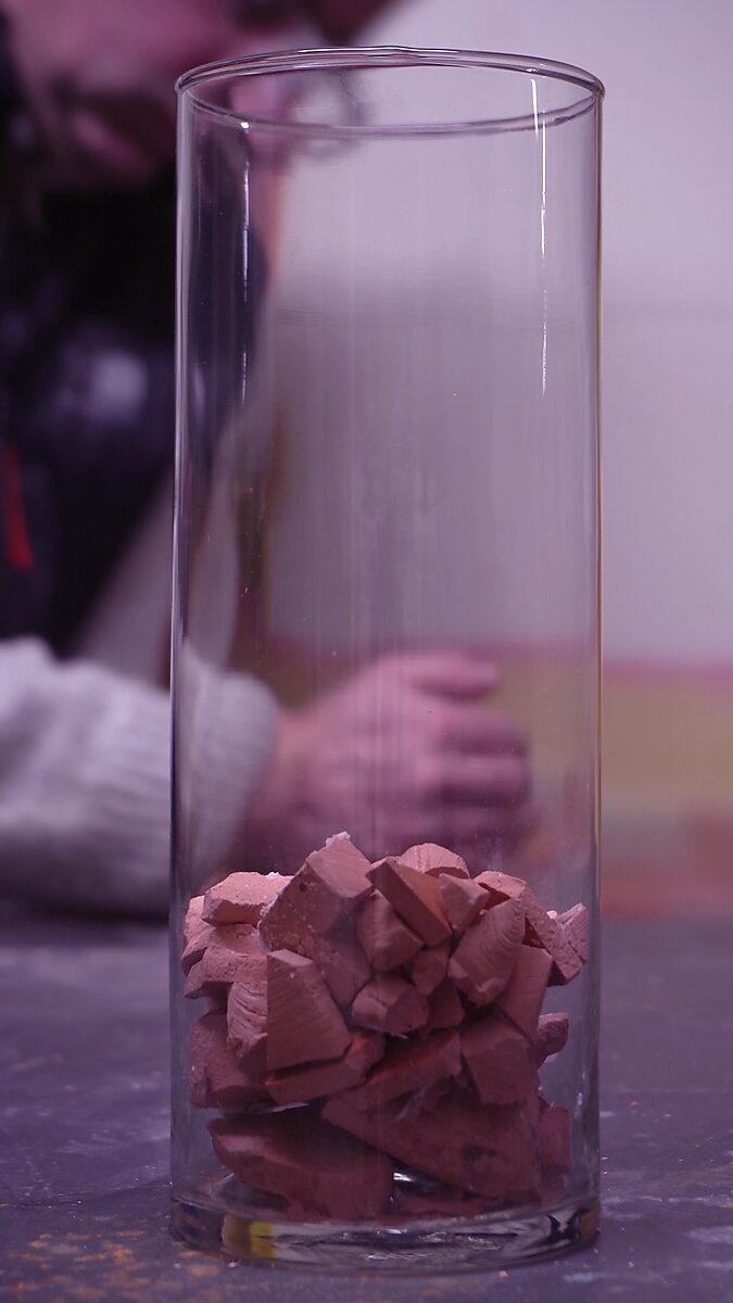 Broken Volume — videostill in which the fragments accumulate into a compact mass at the bottom of the cylinder.
