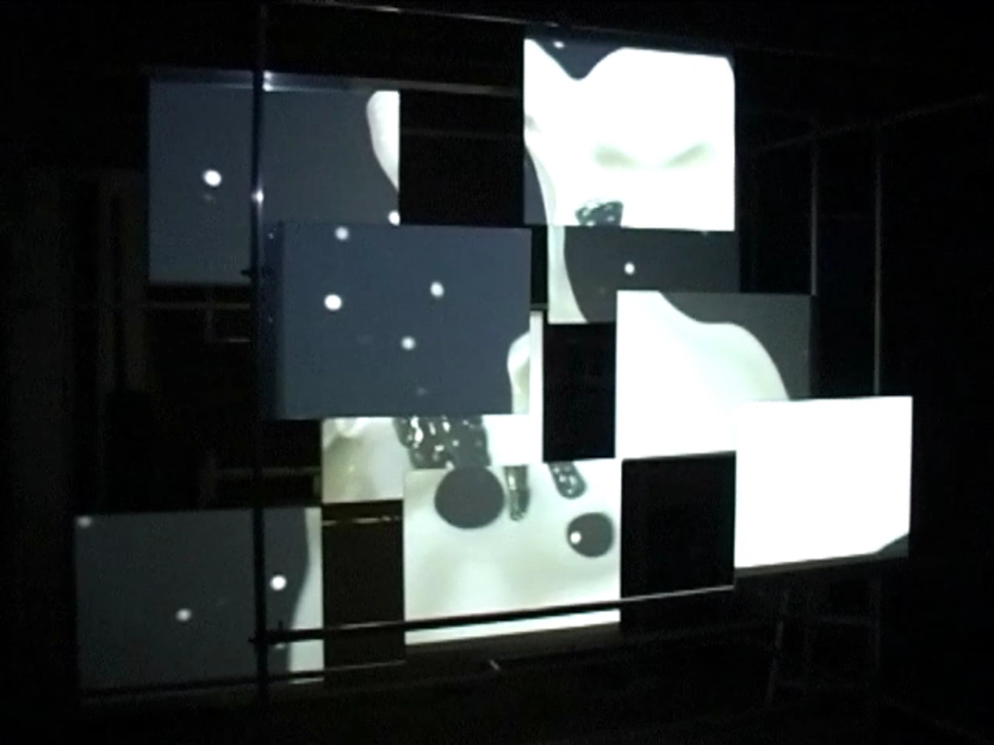 Liquid Forms Through Space — videostill of the installation where high-contrast black and white shapes and circular elements appear across the panels and are split into fragments by the spatial arrangement.