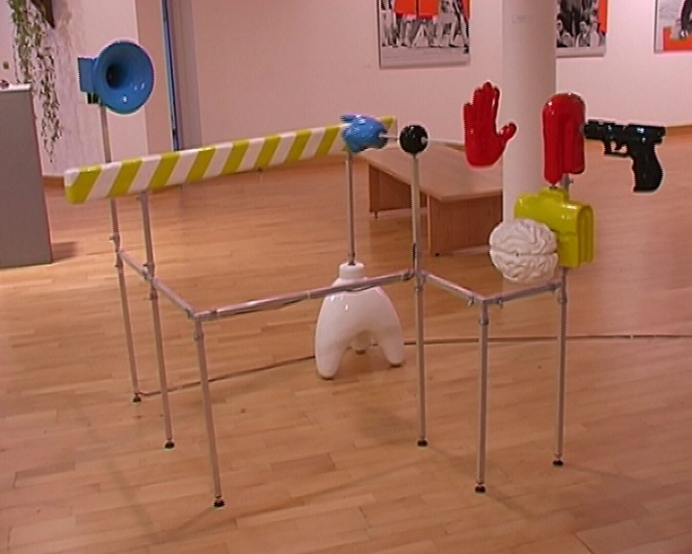 Choose and Change, The Border Speech — photo of the installation: installation with metal rods and various colored objects, including a red U-shaped element, a white sculpture, and a blue object, set in an exhibition space.