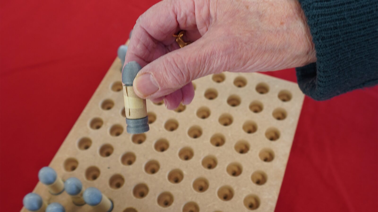 Sfincterman No.0.0 — action videostill: a hand takes a small cylindrical object from a perforated board with holes.
