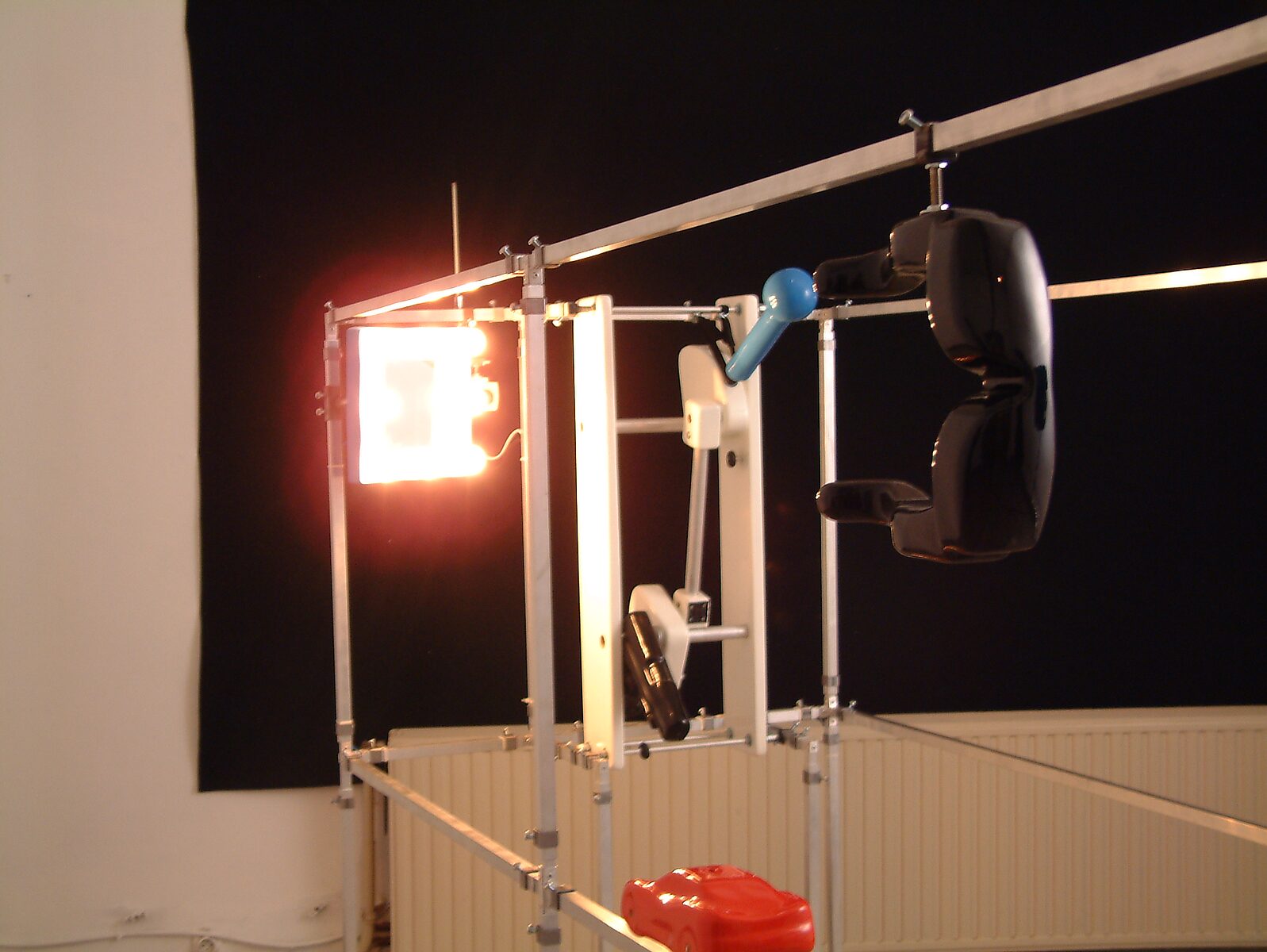 Kies en verander, Installatie voor een egoïstische rapper — detailfoto: metalen constructie met lichtbron en zwarte hangende vorm, met mechanisch element centraal.
