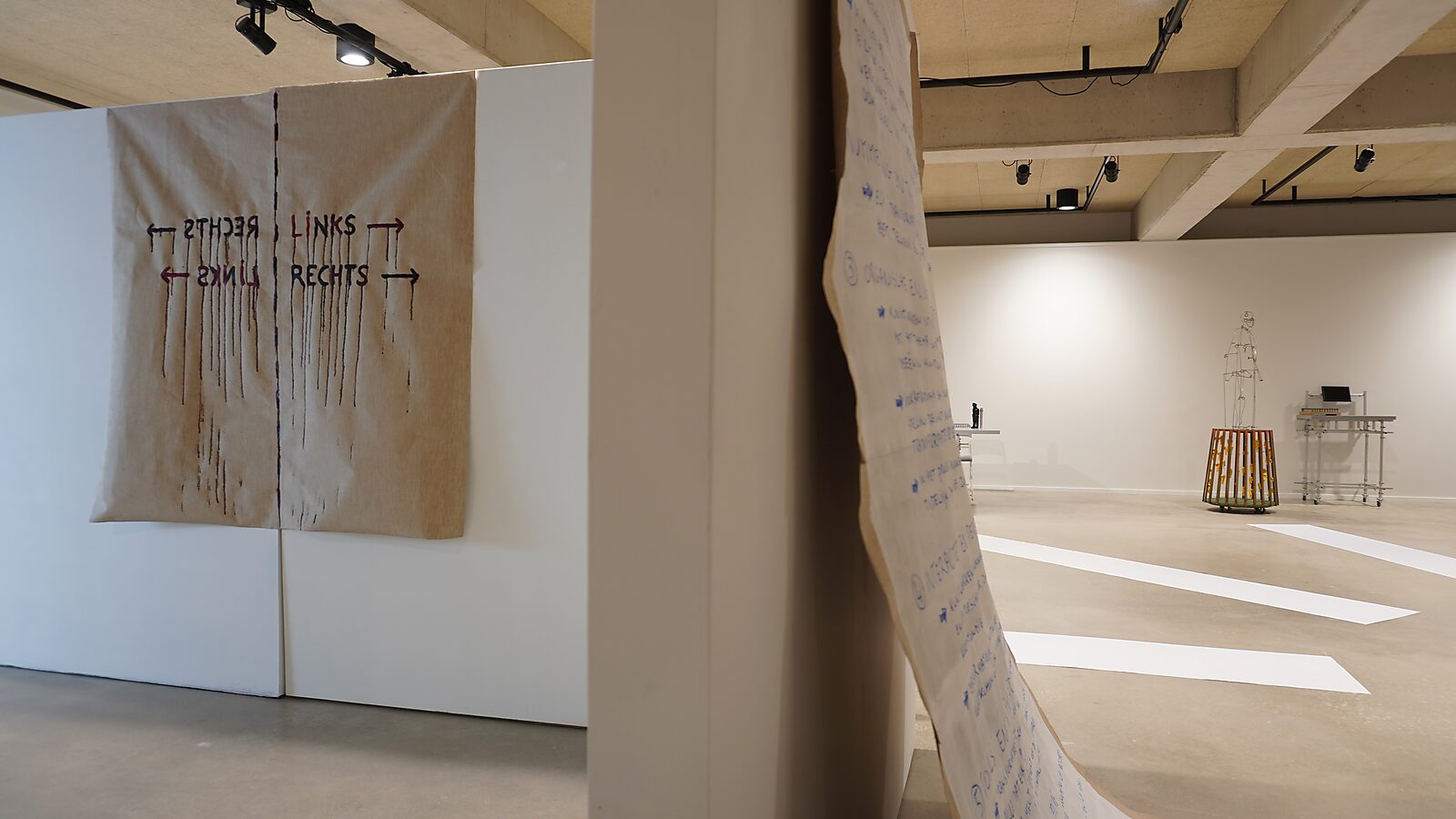 The Divider — process photo: beginning of the canvas during an exhibition — a large canvas with the words “left / right” and arrows hangs in an exhibition space.