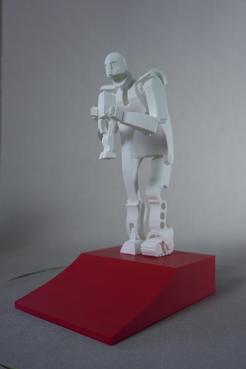 Saturnus — witte 3D-geprinte miniatuur van een staande figuur die een kleinere figuur vasthoudt, geplaatst op een rode hellende sokkel.