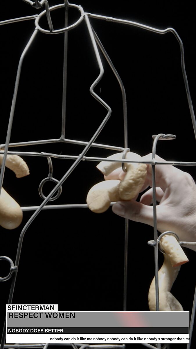 Sfincterman — video work videostill: close-up of the torso with multiple foam forms hanging on the wire frame, as a hand clamps a new form in place.