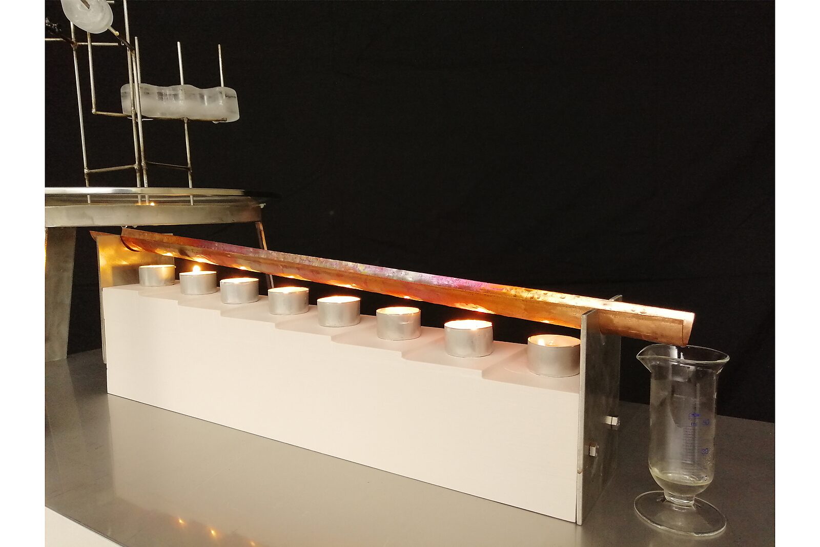 Entropic Sculpture — Aqua Entropica, process photo of the heating gutter with burning tea lights and a glass beaker to collect water.