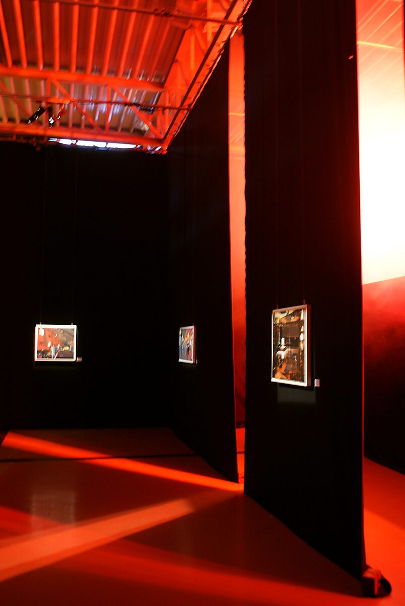 ‘The Modern Cavemen’: Exhibition view with freestanding black curtain panels and suspended oil paintings; intense red light and ceiling structure visible, The Modern Cavemen, Dommelhof, Pelt, 2012.
