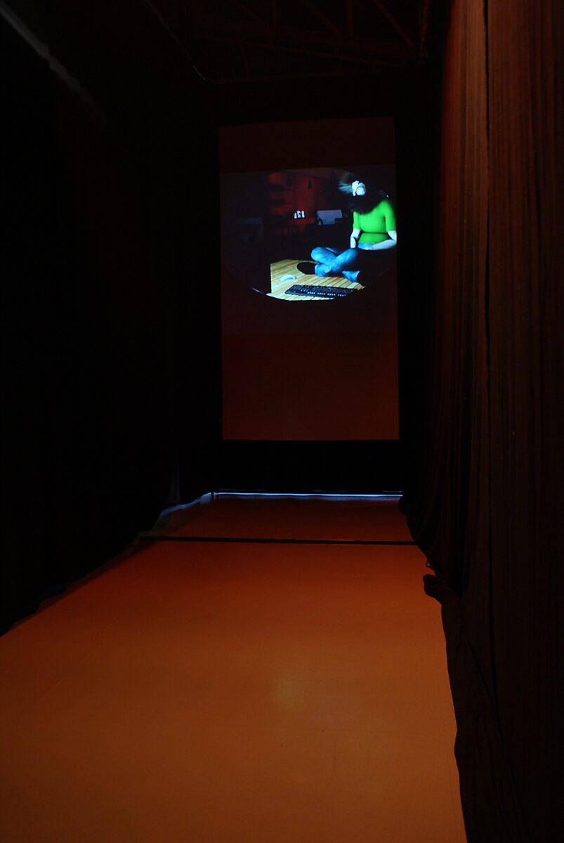 The Modern Cavemen — narrow passage between curtains with a projected image of the modern caveman at the end; the visitor moves as if through a dark cave toward the glow of the screen.