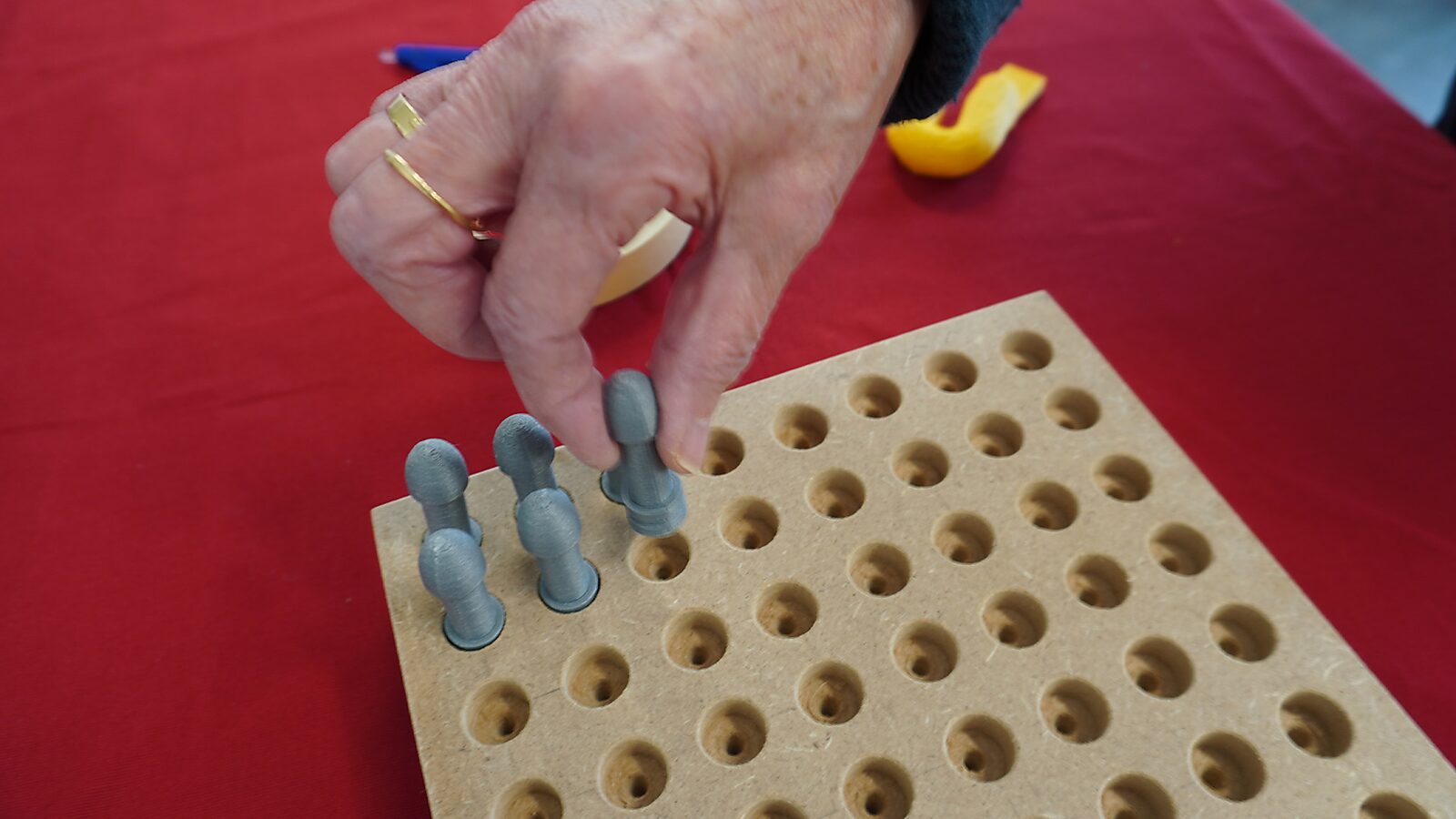 Sfincterman No.0.0 — action videostill: a hand places several small cylindrical objects upright into the perforated board.