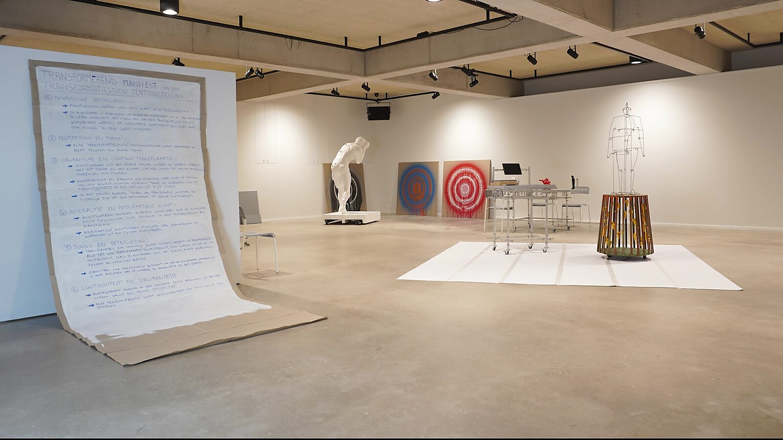 Transformatiestudio nr.1: warm of koud: Tentoonstellingszicht met manifest op de voorgrond en sculpturen op de achtergrond, CC De Adelberg, Lommel, 2024.