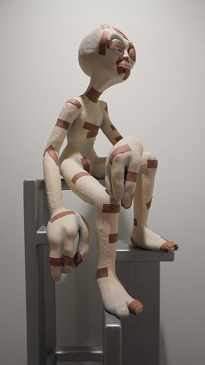 Buitenaardse zorg, pleisterfase 1 — detail: bovenlichaam van de alienfiguur met meerdere bruine pleisters op gezicht, nek en romp; zittend op de grijze stoel.
