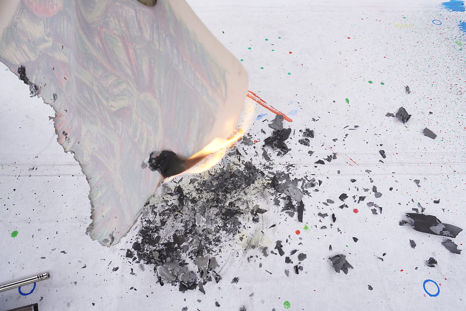 Naming–Value Butterflies — process drawing: Hanging Man (1995) — the burning edge of the paper curls as the flame moves along the drawing; ash and charred pieces scatter across the table.