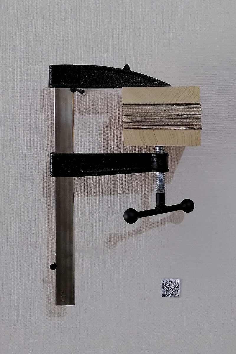 Schilderijen.zip — opnieuw een gecomprimeerd schilderijblok dat tussen houten platen wordt samengeperst door een metalen lijmklem die aan de muur is bevestigd.