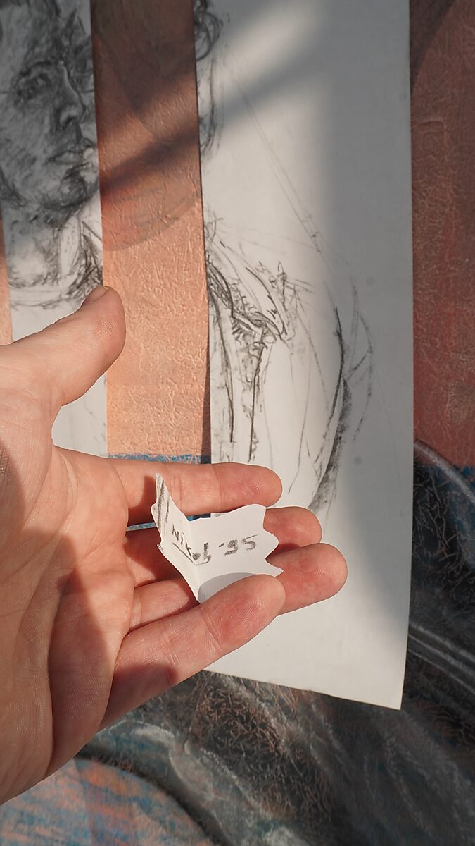 Benoemens-waardvlinders — Naming–Value Butterflies — proces tekening: studie zelfportret (1995), Gevangen (2026) — close-up van het kleine gevouwen vlindervormige stukje papier met de tekst “Niko ’95”.