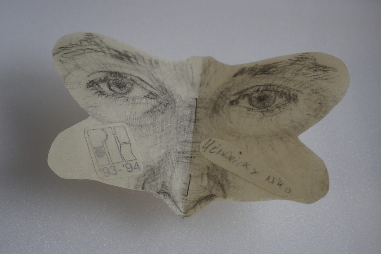 Naming–Value Butterflies — process drawing: study self-portrait 1 PHIKO (1993) — detail of a small butterfly-shaped cut-out with a pencil drawing of eyes and nose; a stamp “PH 93–94” and a handwritten name label appear on the paper.