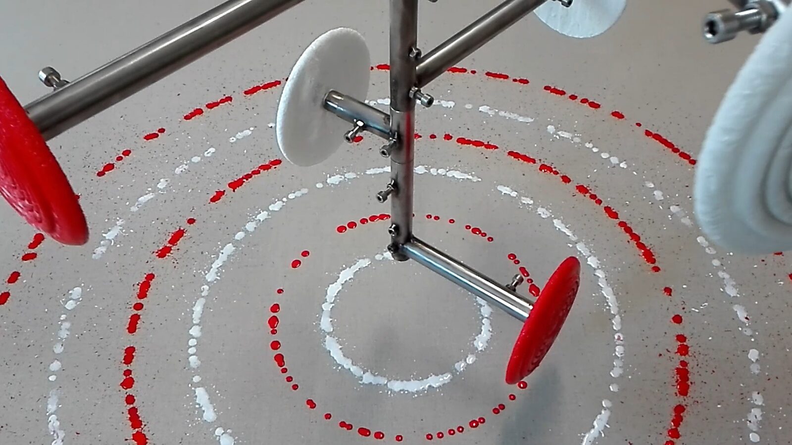 Smeltende doelen nr. 3 — videostill van het druppelproces waarbij roterende ijsdoelen concentrische ringen van rode en witte verf op het doek vormen.