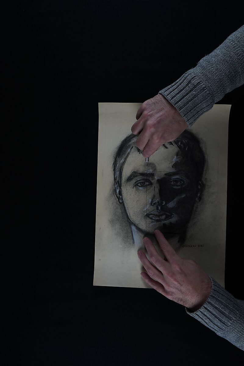 Naming–Value Butterflies — process drawing: self-portrait study 3 PHIKO (1993) — hands cut a small square from the forehead of a charcoal self-portrait using a knife.